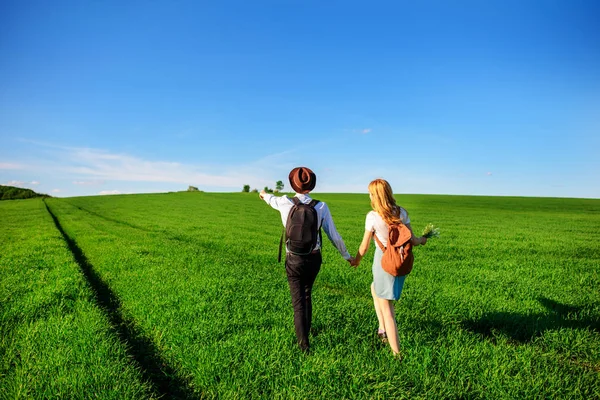 Bir sırt çantası ile bir adam bir şapka ve uzun saçlı bir kadın yol boyunca gidin. Çayır boyunca birkaç yürür.