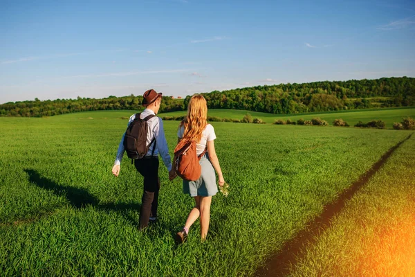 Bir sırt çantası ile bir adam bir şapka ve uzun saçlı bir kadın yol boyunca gidin. Çayır boyunca birkaç yürür.