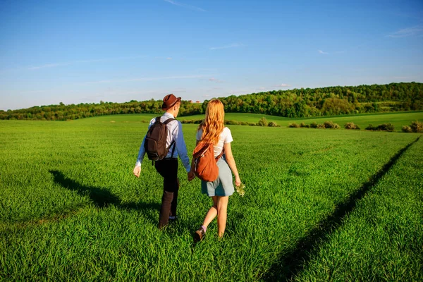 Bir sırt çantası ile bir adam bir şapka ve uzun saçlı bir kadın yol boyunca gidin. Çayır boyunca birkaç yürür.