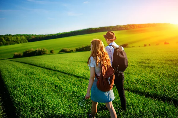 Bir sırt çantası ile bir adam bir şapka ve uzun saçlı bir kadın yol boyunca gidin. Çayır boyunca birkaç yürür.