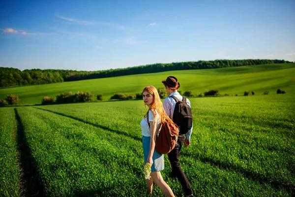 Bir sırt çantası ile bir adam bir şapka ve uzun saçlı bir kadın yol boyunca gidin. Çayır boyunca birkaç yürür.