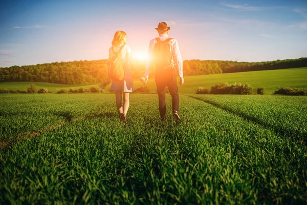 Bir sırt çantası ile bir adam bir şapka ve uzun saçlı bir kadın yol boyunca gidin. Çayır boyunca birkaç yürür.