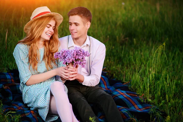 年轻夫妇坐在格子中的公园和看看日落 男人给他的女朋友一束紫丁香 — 图库照片