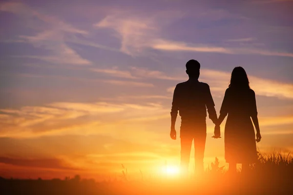 若いカップルが手を繋いでいる日没のシルエットをバックに — ストック写真