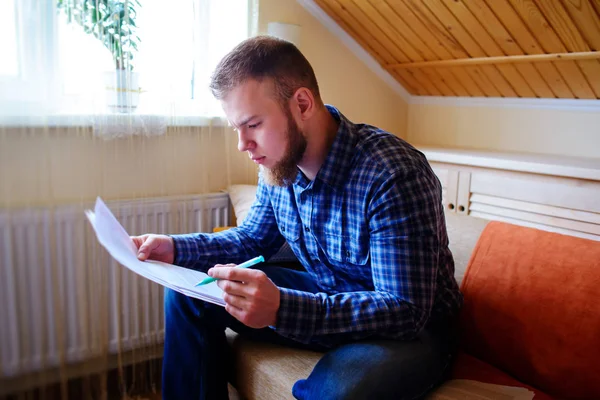 Genç yakışıklı adam kanepede oturan ve bir çalışma kağıdı saatler.