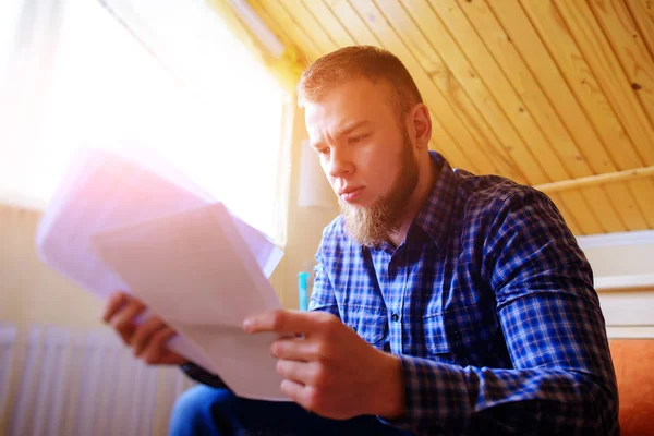 Genç yakışıklı adam kanepede oturan ve bir çalışma kağıdı saatler.