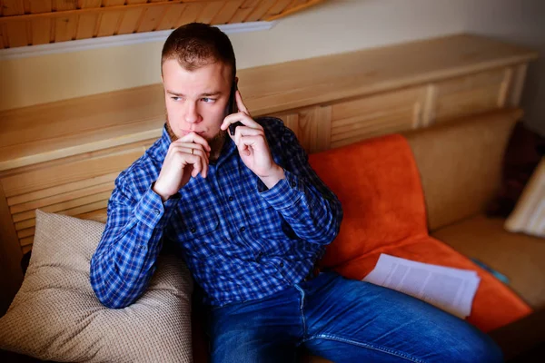 Genç ciddi adam evde kanepede rahat oturan onun telefonda konuşuyor.