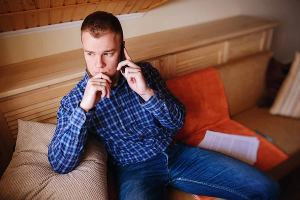 Genç ciddi adam evde kanepede rahat oturan onun telefonda konuşuyor.