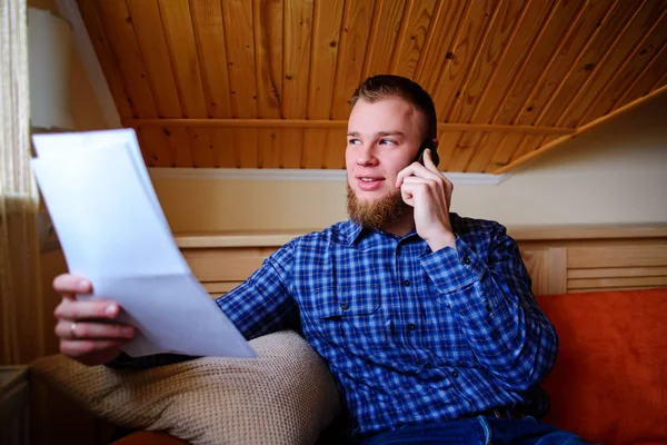 Kağıt basılı tutup evde kanepede otururken cep telefonda konuşurken ciddi olgun adam