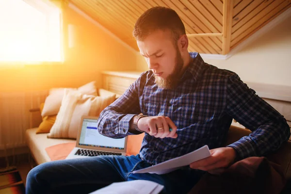 Genç adam eve bir dizüstü bilgisayarda çalışırken belgeleri tutan bir kanepede oturan eğitim.