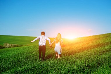 Mutlu aşıklar çayır yeşil çim ve arkasından mavi gökyüzü ile çalışan.