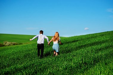 Mutlu aşıklar çayır yeşil çim ve arkasından mavi gökyüzü ile çalışan.