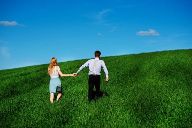 Mutlu aşıklar çayır yeşil çim ve arkasından mavi gökyüzü ile çalışan.