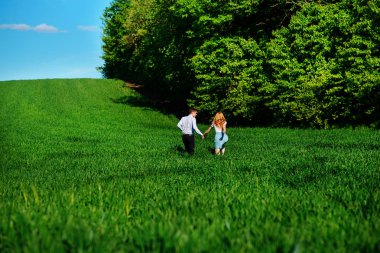 Mutlu aşıklar çayır yeşil çim ve arkasından mavi gökyüzü ile çalışan.