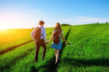 Bir sırt çantası ile bir adam bir şapka ve uzun saçlı bir kadın yol boyunca gidin. Çayır boyunca birkaç yürür.