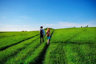 Bir sırt çantası ile bir adam bir şapka ve uzun saçlı bir kadın yol boyunca gidin. Çayır boyunca birkaç yürür.