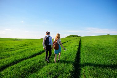 Bir sırt çantası ile bir adam bir şapka ve uzun saçlı bir kadın yol boyunca gidin. Çayır boyunca birkaç yürür.