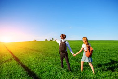 Bir sırt çantası ile bir adam bir şapka ve uzun saçlı bir kadın yol boyunca gidin. Çayır boyunca birkaç yürür.