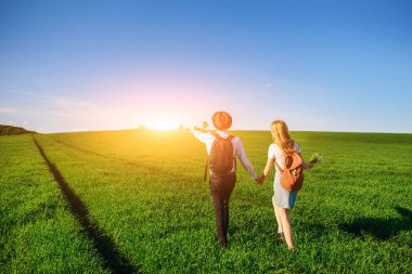 Bir sırt çantası ile bir adam bir şapka ve uzun saçlı bir kadın yol boyunca gidin. Çayır boyunca birkaç yürür.