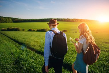 Bir sırt çantası ile bir adam bir şapka ve uzun saçlı bir kadın yol boyunca gidin. Çayır boyunca birkaç yürür.