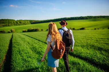 Bir sırt çantası ile bir adam bir şapka ve uzun saçlı bir kadın yol boyunca gidin. Çayır boyunca birkaç yürür.