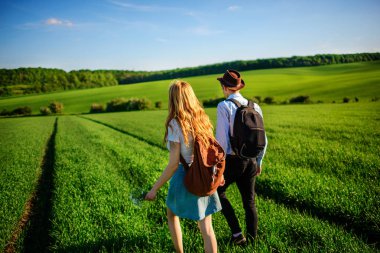 Bir sırt çantası ile bir adam bir şapka ve uzun saçlı bir kadın yol boyunca gidin. Çayır boyunca birkaç yürür.