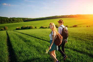 Bir sırt çantası ile bir adam bir şapka ve uzun saçlı bir kadın yol boyunca gidin. Çayır boyunca birkaç yürür.