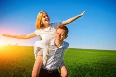 Kollarını dışarı çeker ve arka planı mavi gökyüzü ve yeşil alan bir uçuş taklit eder onun geri mutlu kadın, erkek gülümseyen holding.