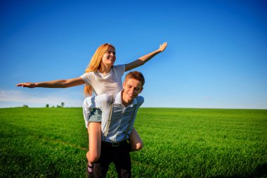 Kollarını dışarı çeker ve arka planı mavi gökyüzü ve yeşil alan bir uçuş taklit eder onun geri mutlu kadın, erkek gülümseyen holding.