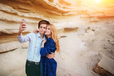 Çekici bir adam güzel bir kadın ile sarılma ve gülümseyerek. Onlar kum ocağı arka plan üzerinde selfie yapıyoruz.