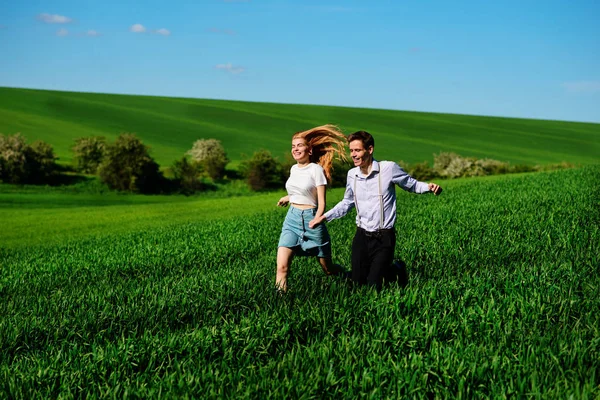 Young happy lovers running on meadow with green grass and blue sky.