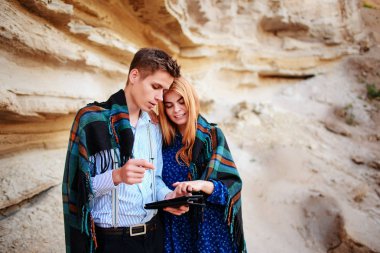 Güzel kadın ve yakışıklı bir battaniyeye sarılmış. Onlar gülümseyen ve bir tablet ekranında bir kum ocağı arka plan üzerinde seyir.