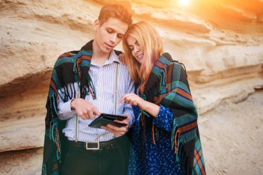 Güzel kadın ve yakışıklı bir battaniyeye sarılmış. Onlar gülümseyen ve bir tablet ekranında bir kum ocağı arka plan üzerinde seyir.