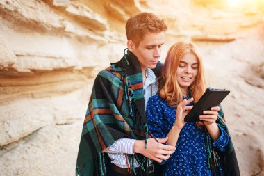 Güzel kadın ve yakışıklı bir battaniyeye sarılmış. Onlar gülümseyen ve bir tablet ekranında bir kum ocağı arka plan üzerinde seyir.