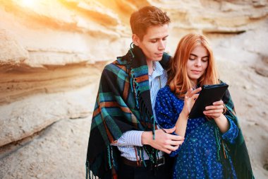 Güzel kadın ve yakışıklı bir battaniyeye sarılmış. Onlar gülümseyen ve bir tablet ekranında bir kum ocağı arka plan üzerinde seyir.