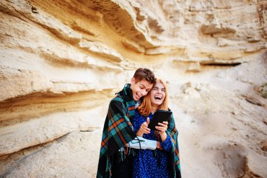 Güzel kadın ve yakışıklı bir battaniyeye sarılmış. Onlar gülümseyen ve bir tablet ekranında bir kum ocağı arka plan üzerinde seyir.