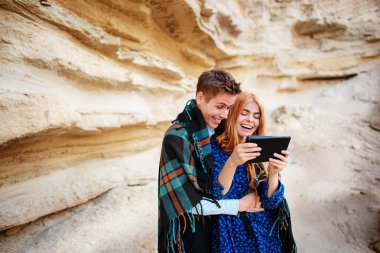 Güzel kadın ve yakışıklı bir battaniyeye sarılmış. Onlar gülümseyen ve bir tablet ekranında bir kum ocağı arka plan üzerinde seyir.