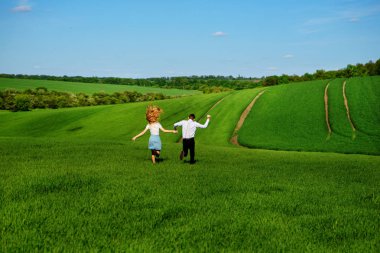 Mutlu aşıklar çayır yeşil çim ve arkasından mavi gökyüzü ile çalışan.