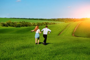 Mutlu aşıklar çayır yeşil çim ve arkasından mavi gökyüzü ile çalışan.