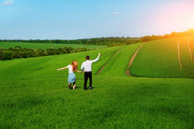 Mutlu aşıklar çayır yeşil çim ve arkasından mavi gökyüzü ile çalışan.