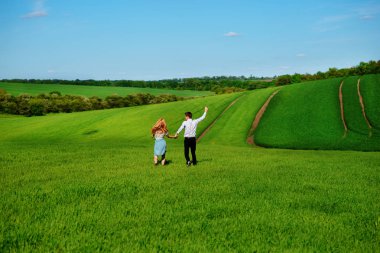 Mutlu aşıklar çayır yeşil çim ve arkasından mavi gökyüzü ile çalışan.