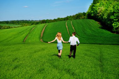 Mutlu aşıklar çayır yeşil çim ve arkasından mavi gökyüzü ile çalışan.
