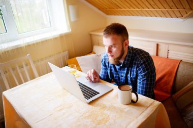 Onun laptop içinde internette sörf rahat genç profesyonel bir yemek odası.