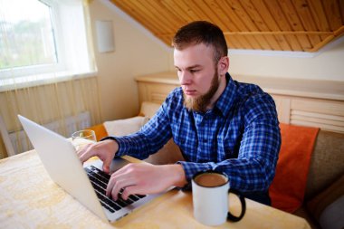 Onun laptop içinde internette sörf rahat genç profesyonel bir yemek odası.