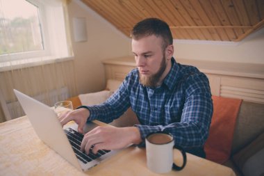 Onun laptop içinde internette sörf rahat genç profesyonel bir yemek odası.