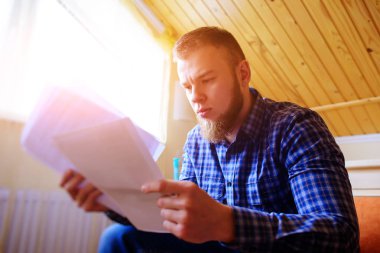 Genç yakışıklı adam kanepede oturan ve bir çalışma kağıdı saatler.