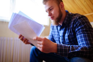 Genç yakışıklı adam kanepede oturan ve bir çalışma kağıdı saatler.