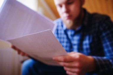 Genç yakışıklı adam kanepede oturan ve bir çalışma kağıdı saatler.