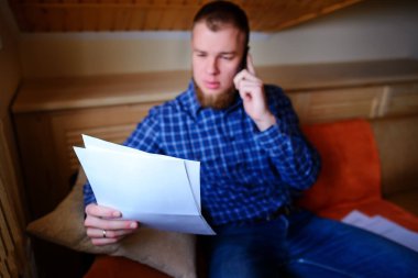 Kağıt basılı tutup evde kanepede otururken cep telefonda konuşurken ciddi olgun adam