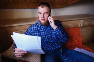 Kağıt basılı tutup evde kanepede otururken cep telefonda konuşurken ciddi olgun adam